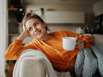Junge Frau sitzt mit Kaffeetasse auf der Couch | © Getty Images/Halfpoint Images