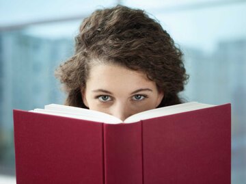 Frau blickt hinter einem Buch hervor | © Getty Images/Westend61