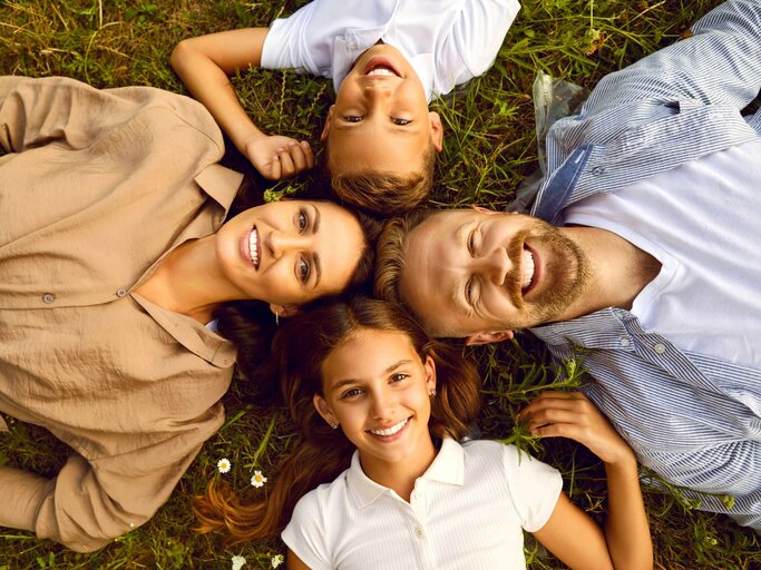 vierköpfige Familie von oben fotografiert liegt auf der Wiese | © Adobe Stock/Studio Romantic