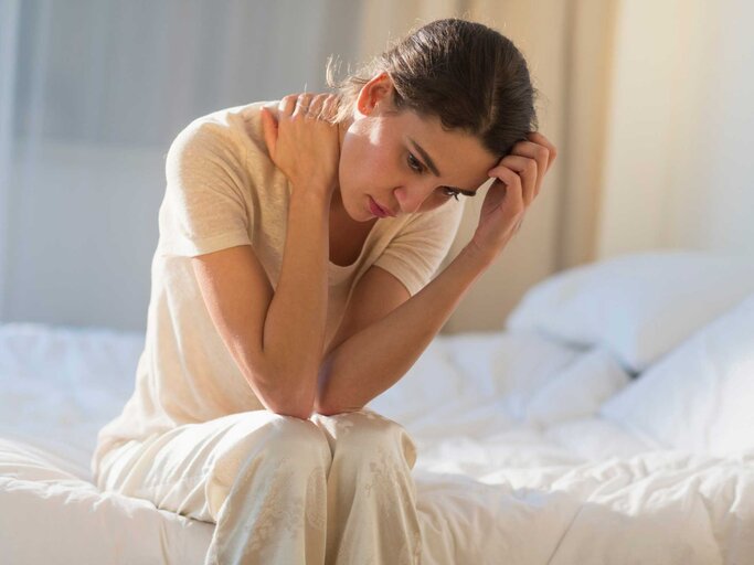 Frau sitzt nachdenklich auf ihrem Bett | © Getty Images/Tetra Images