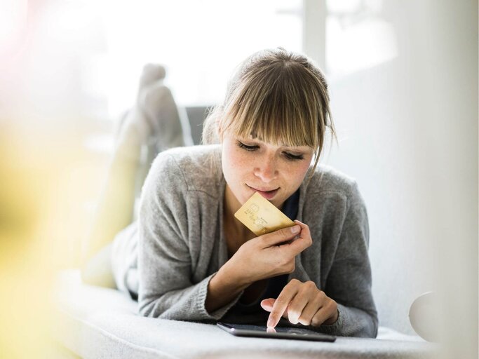 Person mit Kreditkatrte und Tablet auf Sofa | © Getty Images/Westend61