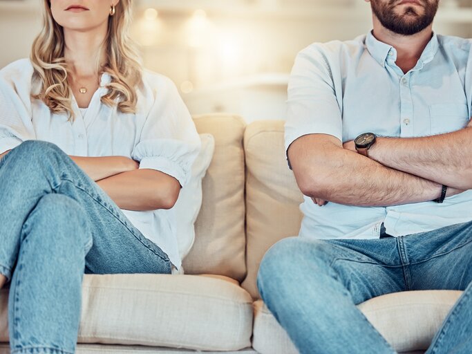 Mann und Frau sitzen mit verschränkten Armen nebeneinander auf dem Sofa | © AdobeStock/peopleimages.com/Clement C