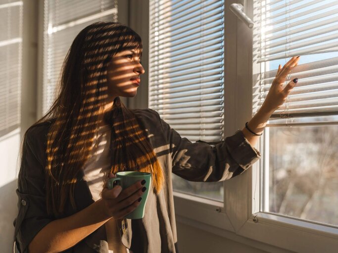 Person sieht besorgt aus Fenster | © Getty Images/Milena Magazin