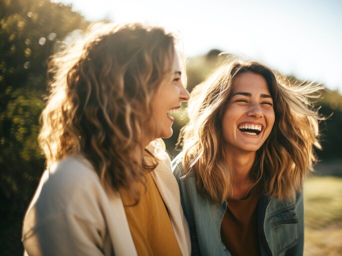  Zwei blonde junge Frauen lachen und haben gemeinsam Spaß in der Natur | © Adobe Stock/Axel Bueckert/Generiert mit KI