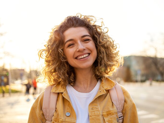  Porträt einer jungen Frau mit lockigem Haar in der Stadt | © Adobe Stock/pikselstock