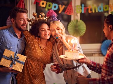 Eine Gruppe von Menschen feiert Geburtstag mit Hüten, Kuchen und Geschenk. | © Adobe Stock/luckybusiness