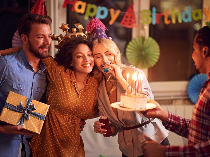 Eine Gruppe von Menschen feiert Geburtstag mit Hüten, Kuchen und Geschenk. | © Adobe Stock/luckybusiness