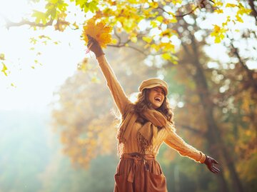  Frau mit gelben Blättern, die draußen im Herbstpark Spaß hat | © Adobe Stock/Alliance