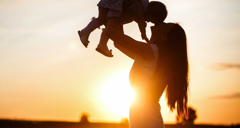 Frau hebt ihr Baby hoch im Sonnenuntergang | © Adobe Stock/Yulia Sugarbox