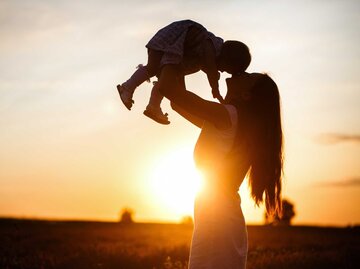 Frau hebt ihr Baby hoch im Sonnenuntergang | © Adobe Stock/Yulia Sugarbox