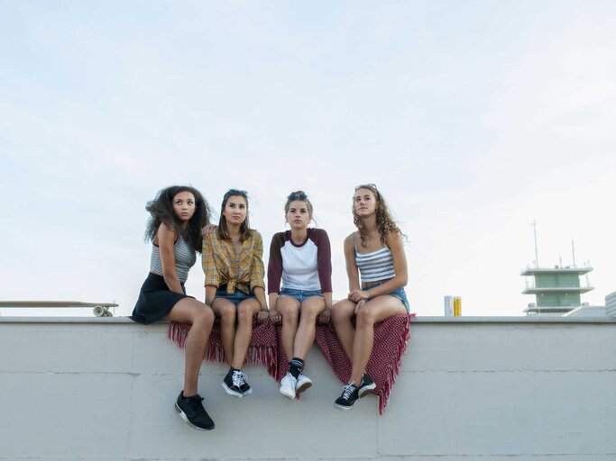 Freundinnen sitzen auf einer Mauer. | © Getty Images/Joos Mind