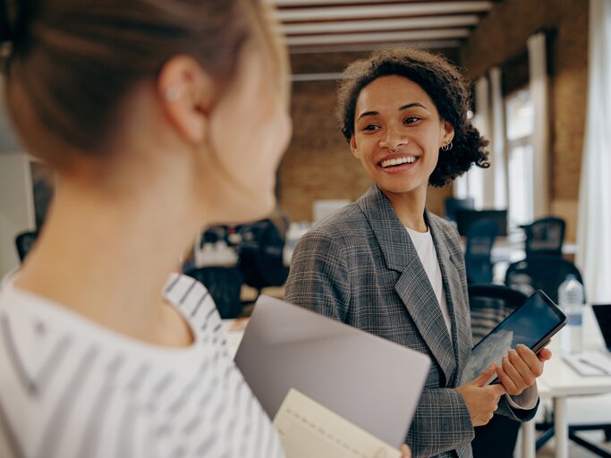 Zwei Arbeitskolleginnen lachen im Büro | © AdobeStock/Daria