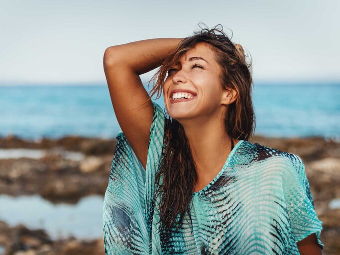 Frau lacht am Strand | © Adobe Stock/milanmarkovic78