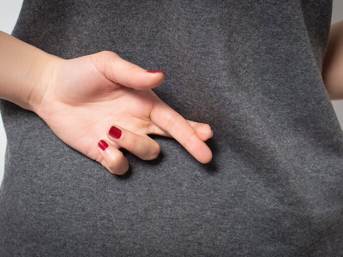 Hand mit roten Fingernägeln und gekreuzten Fingern hinterm Rücken | © Getty Images/Mikhail Azarov