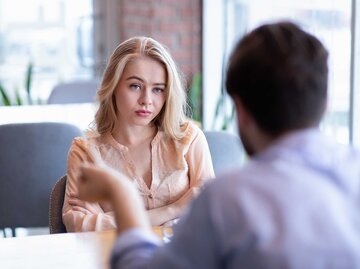 Junges Paar sitzt in einem Café und diskutiert, die Frau hat verschränkte Arme und schaut skeptisch. | © Adobe Stock/Prostock-studio