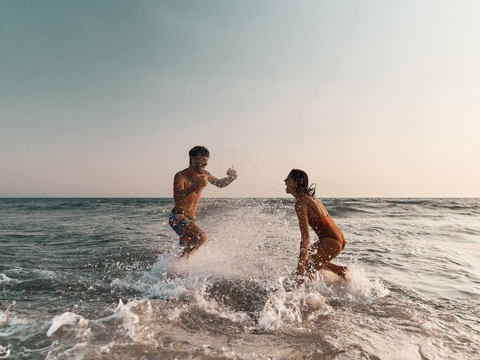 Frau und Mann toben im Meer | © Getty Images/skynesher