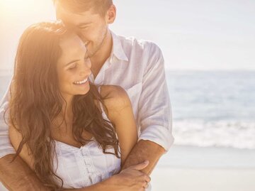 Glückliches junges Paar umarmt sich lachend am Strand. | © Adobe Stock/vectorfusionart