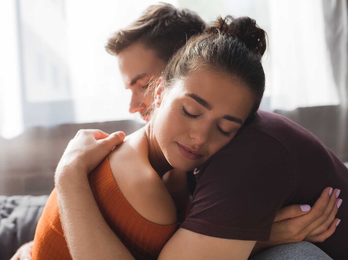 Eine Frau umarmt einen Mann auf der Couch aufgrund von Verlustängsten in der Beziehung. | © Adobe Stock/LIGHTFIELD STUDIOS