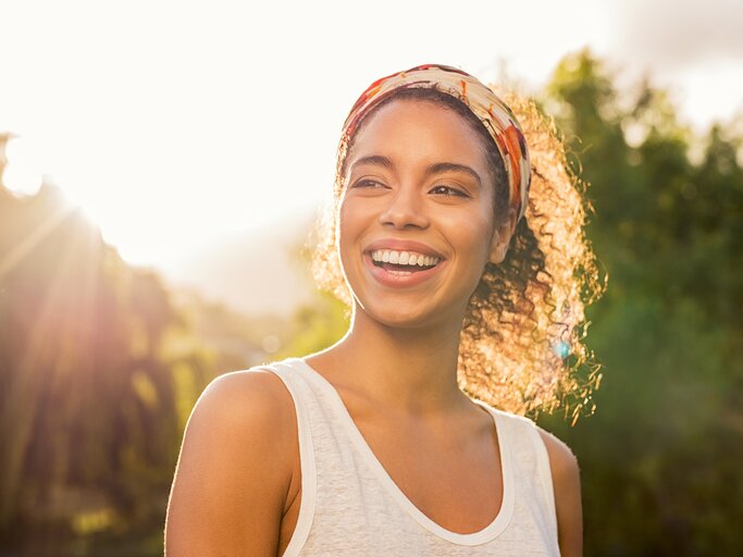  Junge Frau lächelt bei Sonnenuntergang | © Adobe Stock/Rido