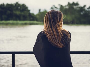 Nachdenkliche Frau steht am Fluss und betrachtet das Wasser. | © Adobe Stock/Kittiphan