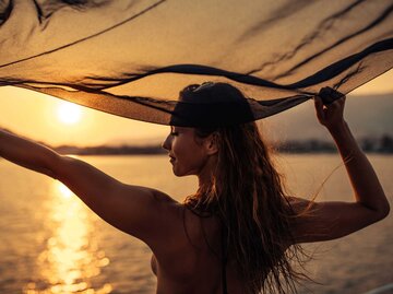 Frau hält ein Tuch hoch bei Sonnenuntergang | © Adobe Stock/bernardbodo