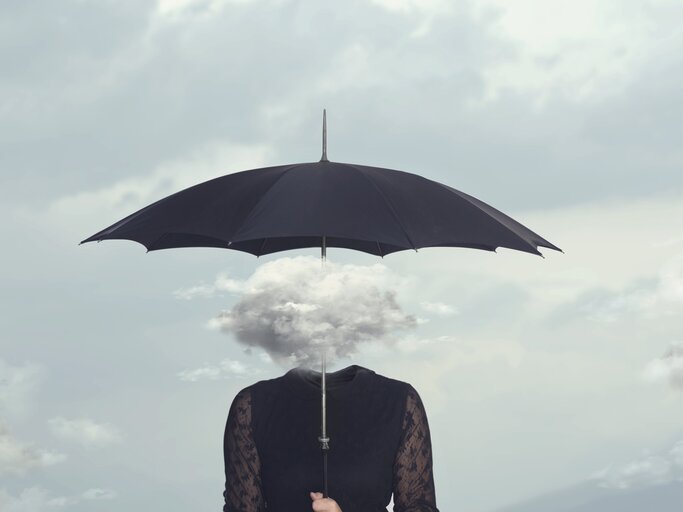 Schwarz gekleideet Frau, die eine Gewitterwolke auf ihrem Kopf trägt und einen Regenschirm aufgespannt hat | © GettyImages/fcscafeine