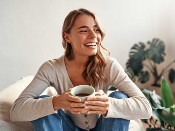 Frau lacht gelassen mit einer Tasse Tee. | © Getty Images/Valerii Apetroaiei