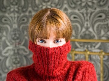 Junge Frau hat sich den Rollkragen über die Hälfte ihres Gesichts gezogen. | © Getty Images/Tara Moore