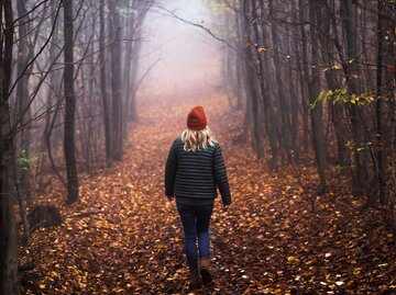 Eine Frau läuft einsam durch einen Wald bei winterlichen Temperaturen. | © Adobe Stock/encierro