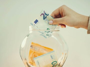 Person legt Geldschein in Glasgefäß | © Getty Images/Vitalii Petrushenko