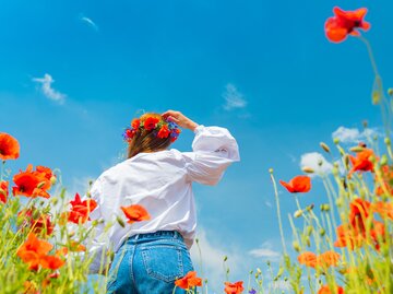 Junge Frau steht in Blumenfeld aus Mohn | © GettyImages/GarryKillian