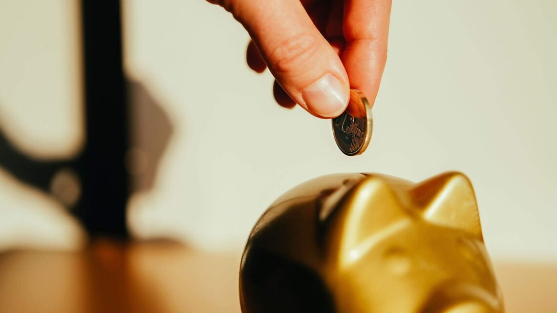 Hand mit Münze und Sparschwein | © Getty Images/Guido Mieth