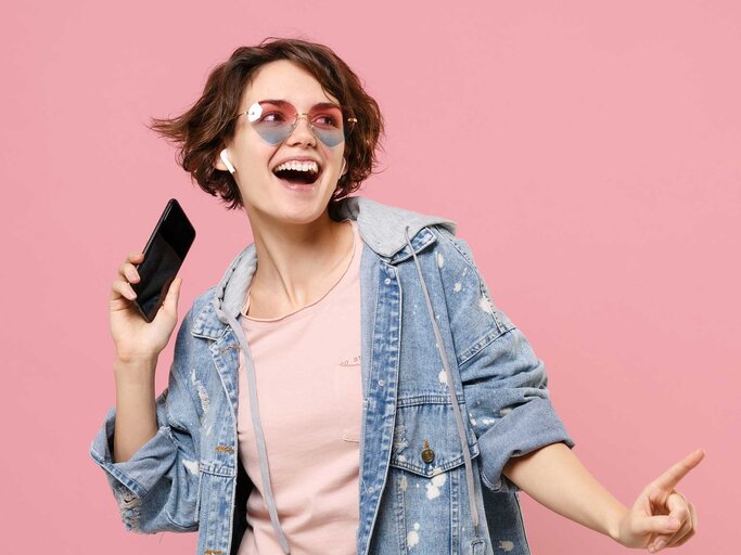 Frau tanzt mit AirPods in den Ohren und einem iPhone in der Hand. | © Getty Images / ViDi Studio