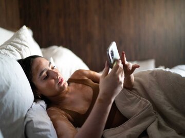 Junge Frau liegt im Bett und schreibt eine Nachricht auf ihrem Handy | © Getty Images/FG Trade