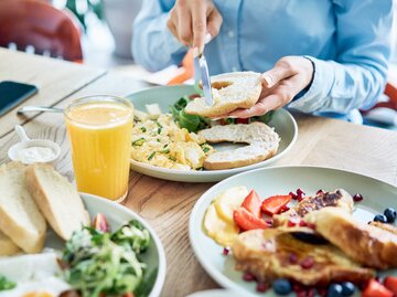 Close up von einer Frau, die im Café frühstückt, vor ihr ein reichlich gedeckter Tisch mit gesundem Frühstück. | © Adobe Stock/baranq