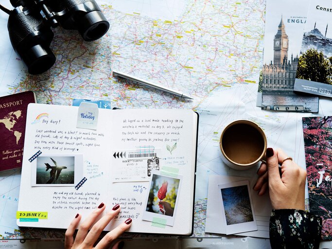 Hände von oben fotografiert auf einer Weltkarte mit Notizbuch | © gettyimages.de | Rawpixel