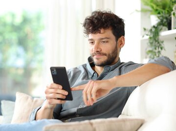 Mann benutzt sein Handy und sitzt auf der Couch | © Getty Images/Antonioguillem
