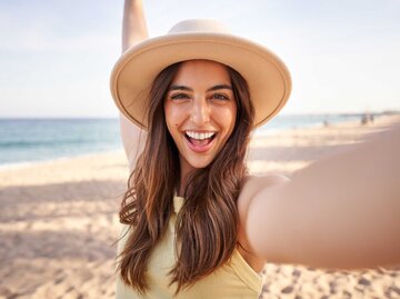 Strahlende Frau macht ein Selfie am Strand | © Getty Images/Carlos Barquero