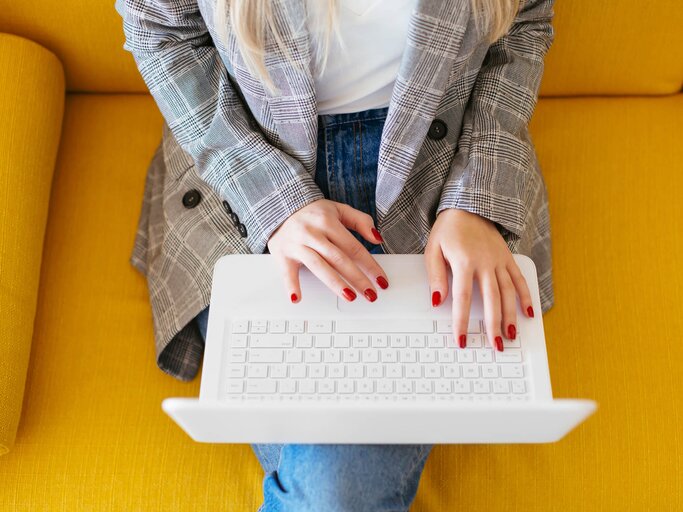 Businessfrau sitzt auf einer gelben Couch und arbeitet am Laptop | © gettyimages.de / Westend61