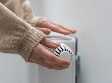 Hand einer Frau greift an das Thermostat der Heizung | © Adobe Stock/Angelov