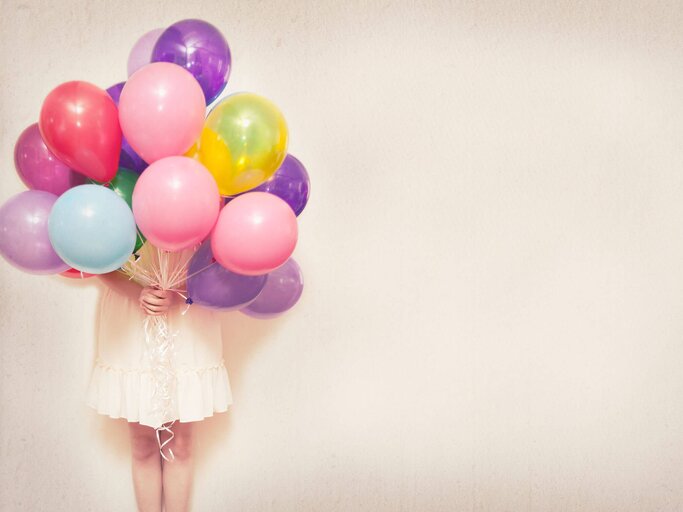 Frau verdeckt Kopf mit vielen Luftballons | © Getty Images/left of centre photography