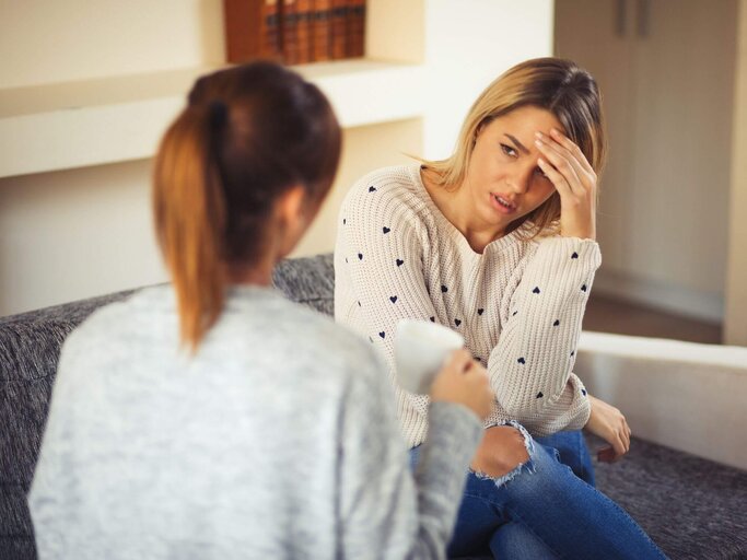 Zwei Frauen unterhalten sich ernst auf einer Couch | © Getty Images/Emir Memedovski