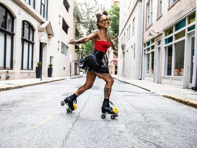 Frau trägt einen schwarzen Rock und ein rotes Top mit einer gelben Sonnenbrille und fährt auf der Straße mit ihren Rollschuhen. | © Getty Images/MoMo Productions