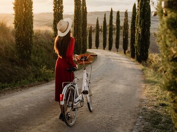 Frau mit Kleid schiebt Fahrrad | © Getty Images/SimonSkafar