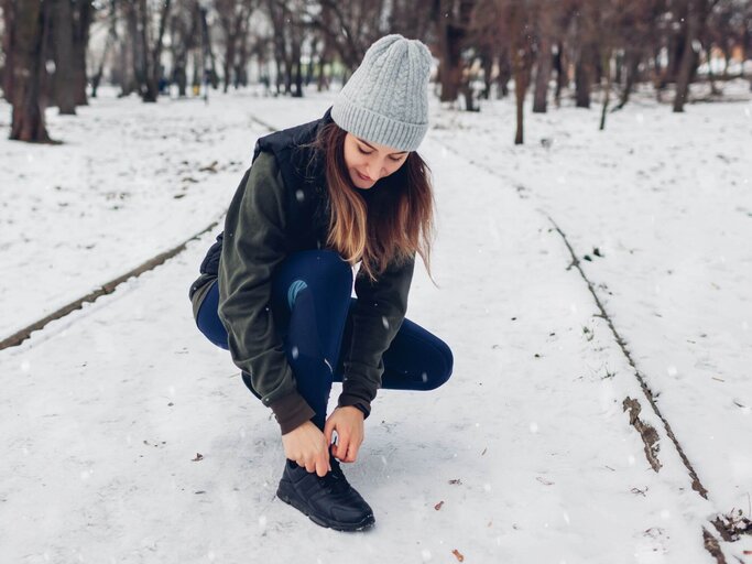 Frau bindet sich Sneaker im Schnee | © Getty Images/Maryviolet