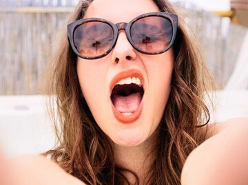 Junge Frau mit Sonnenbrille macht frech ein Selfie. | © Getty Images/georgeclerk