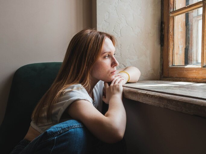 Person sitzt traurig vor Fenster. | © Getty Images/MementoJpeg