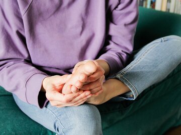Eine Person sitzt und hält den Fuß in den Händen. | © GettyImages/Kinga Krzeminska