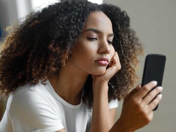Junge Frau schaut gelangweilt auf ihr Handy | © Getty Images/bymuratdeniz