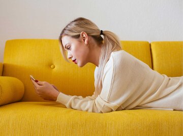 Frau liegt auf der Couch und scrollt auf ihrem Handy | © Getty Images/Westend61
